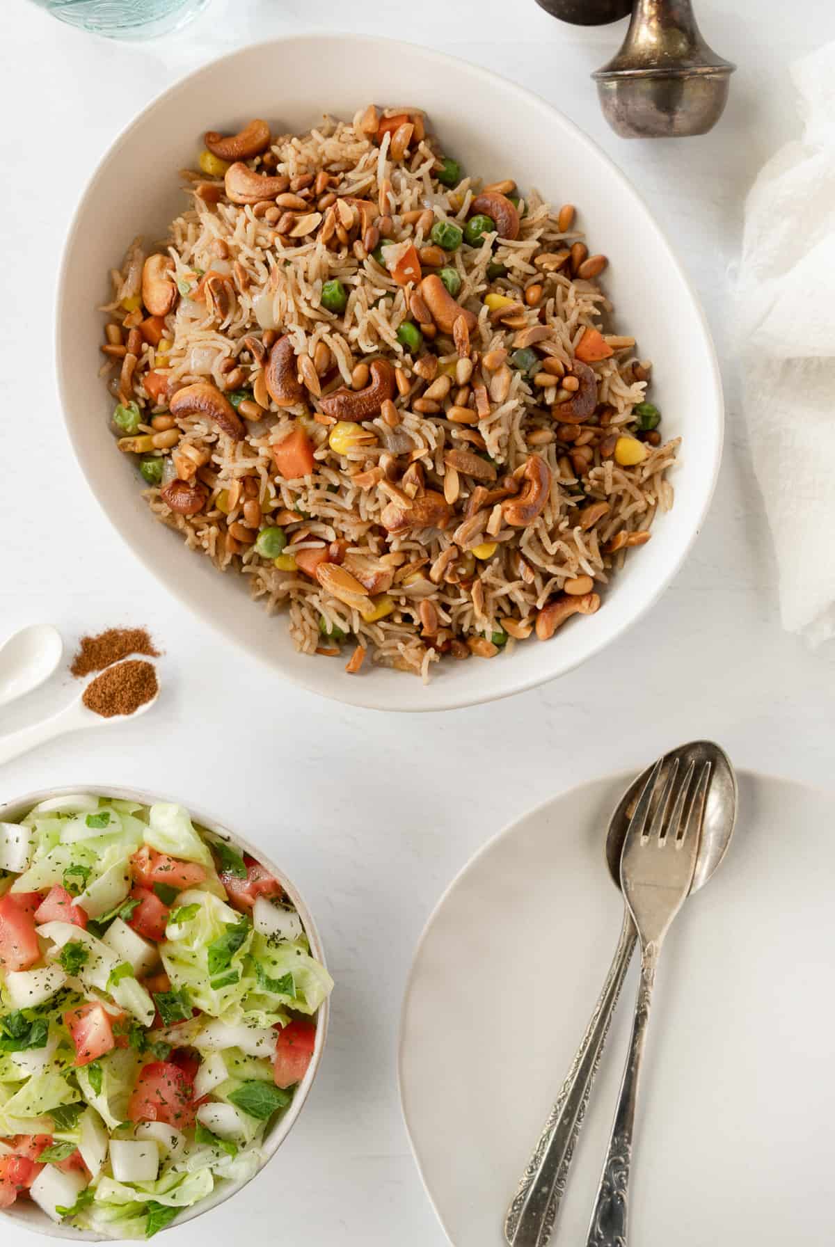 a white bowl with spiced rice with toasted nuts and vegetables and a salad on the side