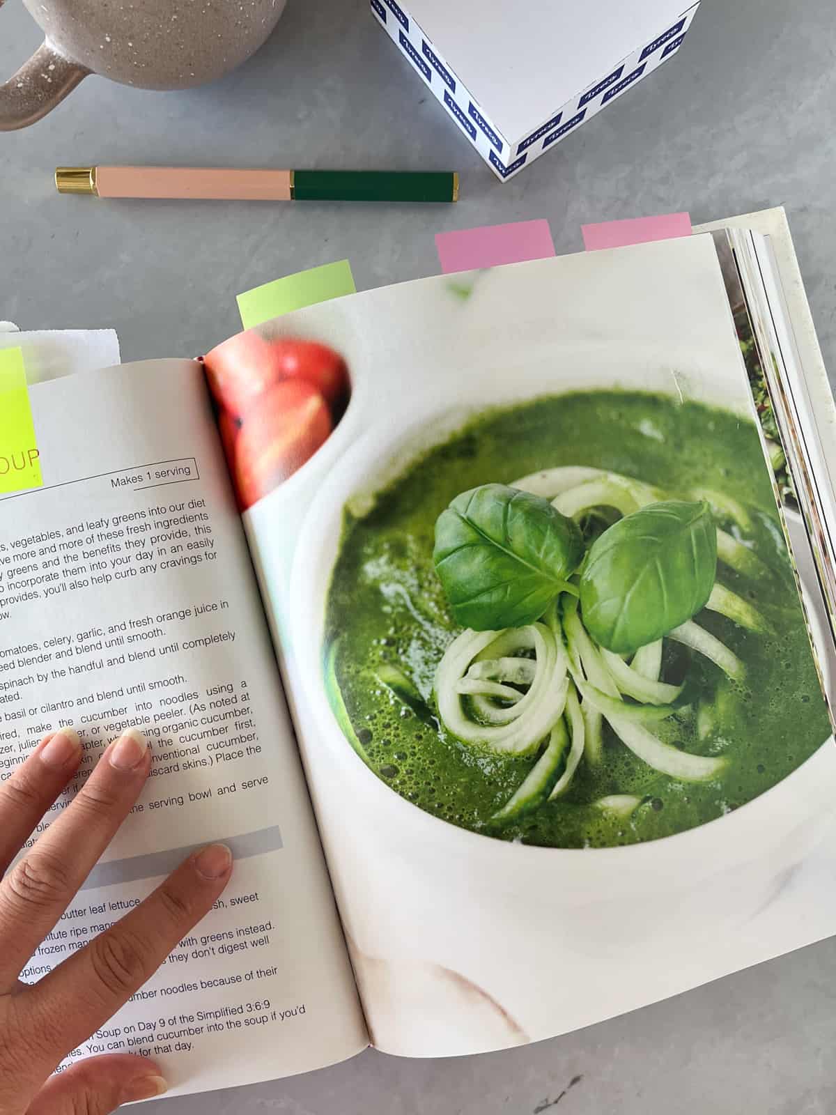 a hand holding open a book on a cold spinach soup recipe