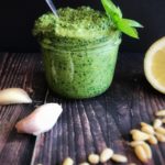 pesto in a glass jar with pine nuts scattered around it