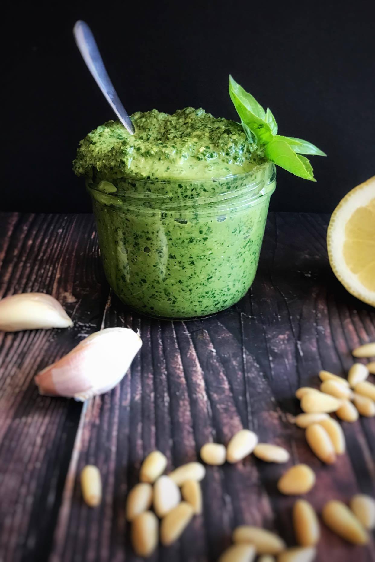 pesto in a glass jar with pine nuts scattered around it