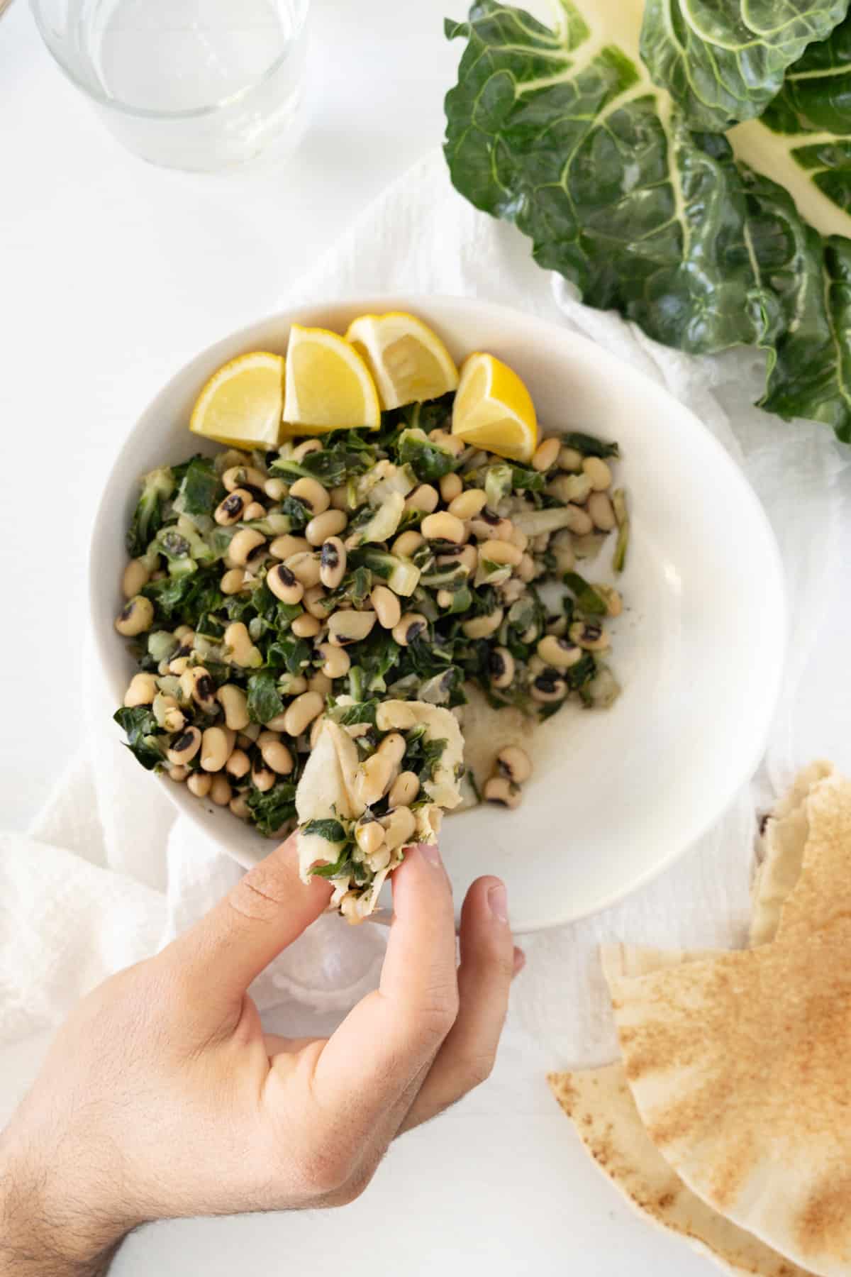 a male hand holding some cooked black eyed peas with swiss chard on top of a plate full of it