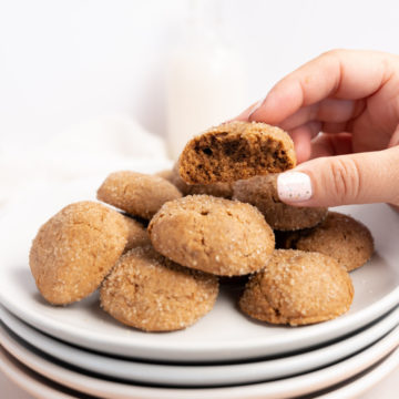 vegan ginger cookies on a stack of plates with a female hand picking one up