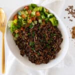 cooked lentils and bulgur called mujadara hamra in a white bowl with a salad
