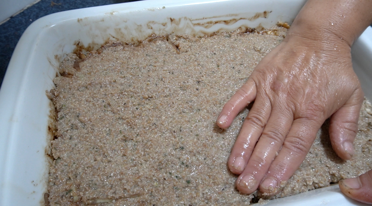 a female hand adding top layer of kibbeh to the bottom layer