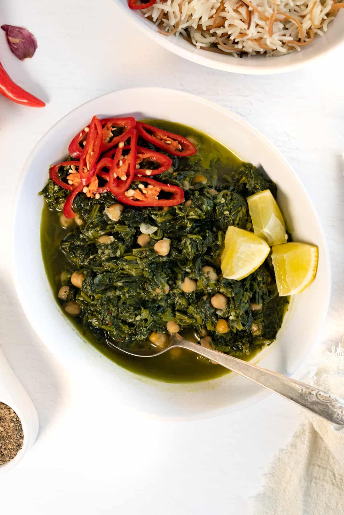 cooked spinach in green both with wedges of lemon in a white bowl