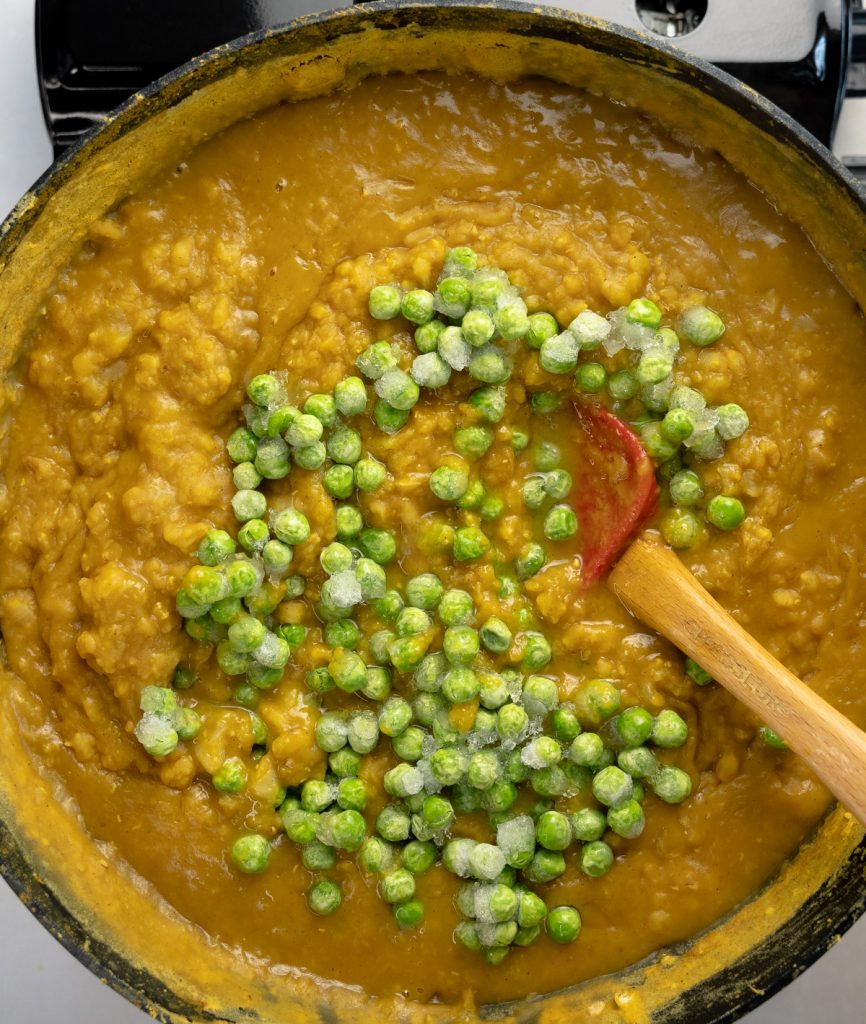 frozen peas added to yellow barley porridge in a pan