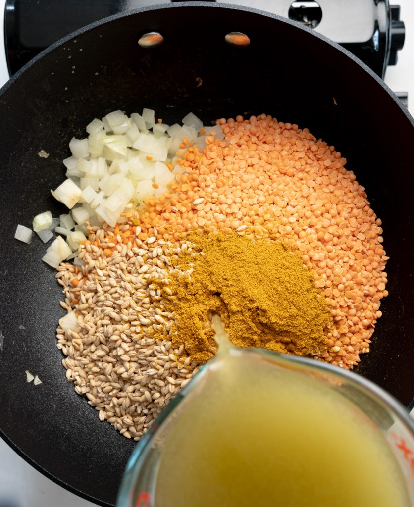adding barley, red lentils, curry powder and stock to the onions in a black frypan