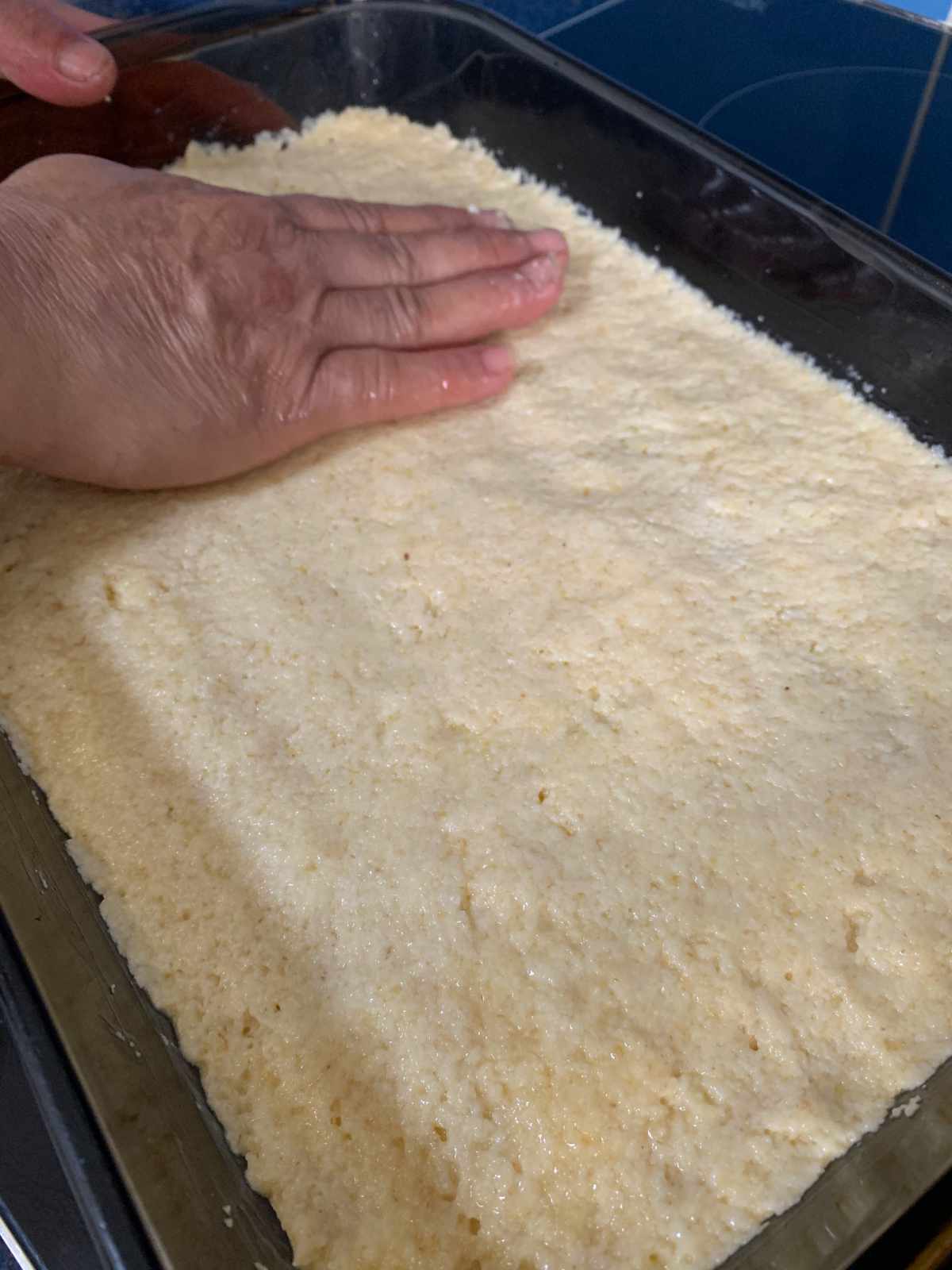 flattening namoura dough by hand into a tray