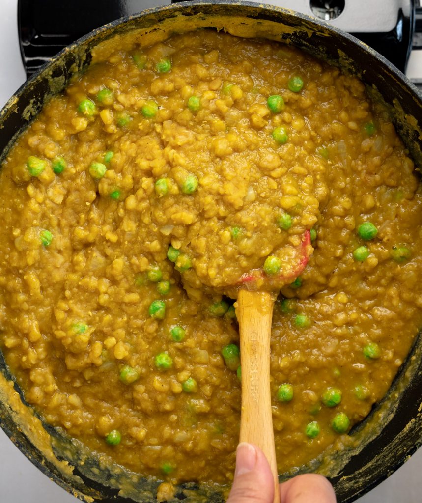 hand stirring frozen peas into the yellow porridge