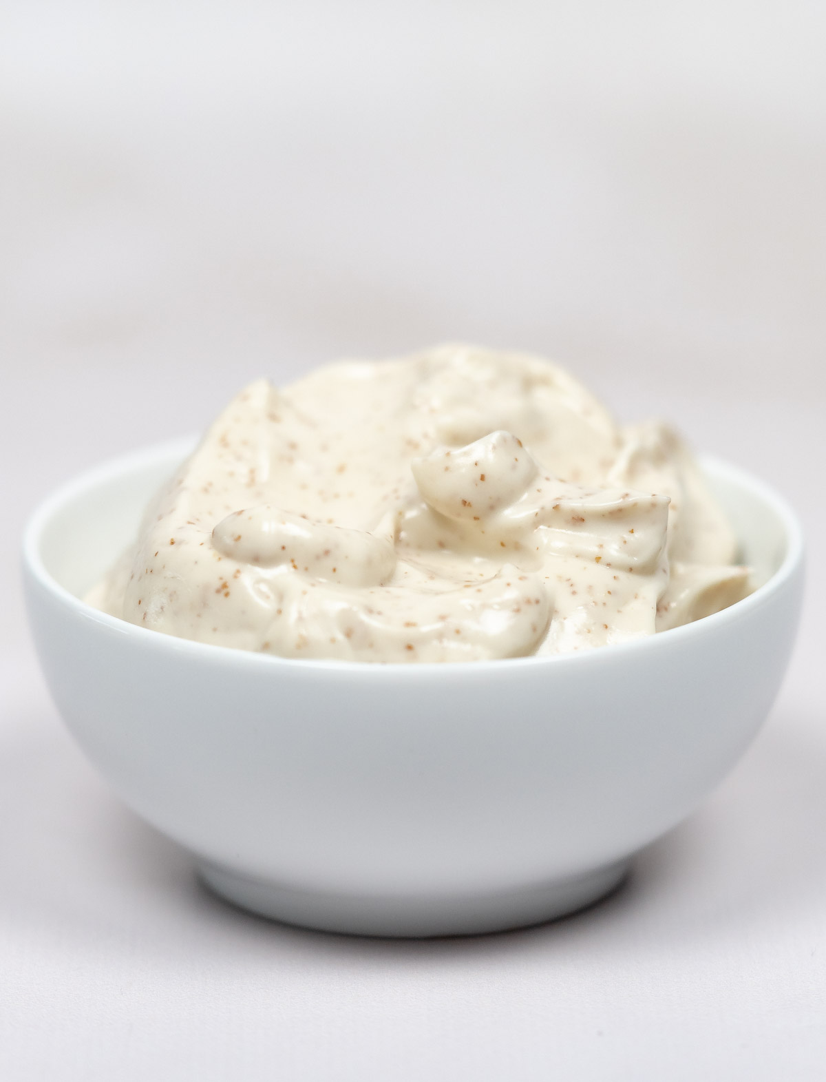 a white bowl of white mayonnaise with light brown specks through it