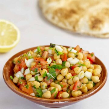 a brown bowl filled with chickpeas, chopped tomato, onion and parsley salad