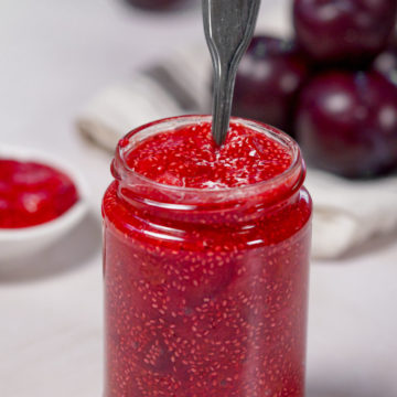sugar free plum jam in a glass jar with plums in the back ground