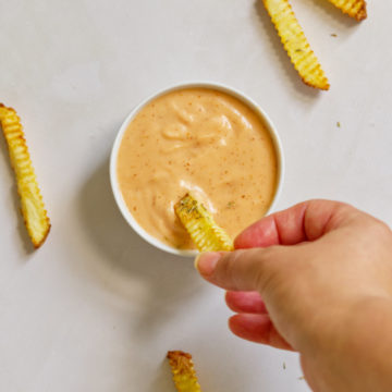 hand dipping french fry into vegan fry sauce