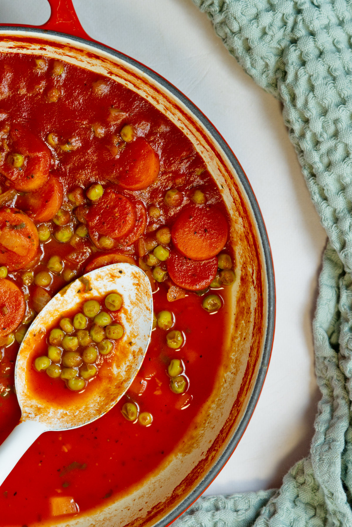 stewed peas and carrots in a red pot with a white spoon