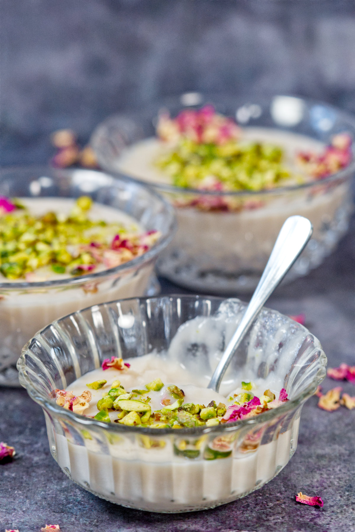 Muhallabi in three bowls with pistachio and rose petal garnish