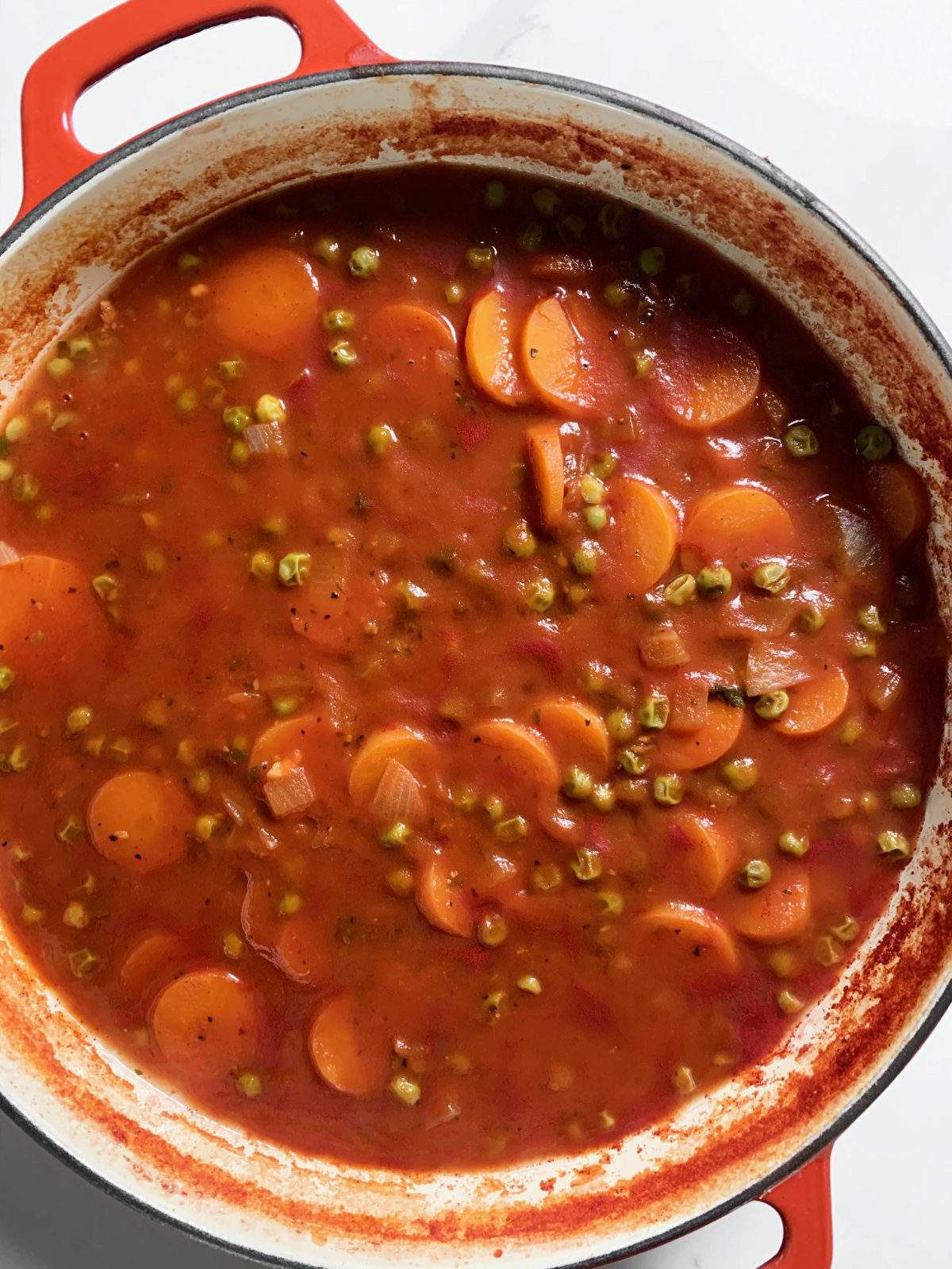 stewed peas and carrots in red sauce in a red casserole dish
