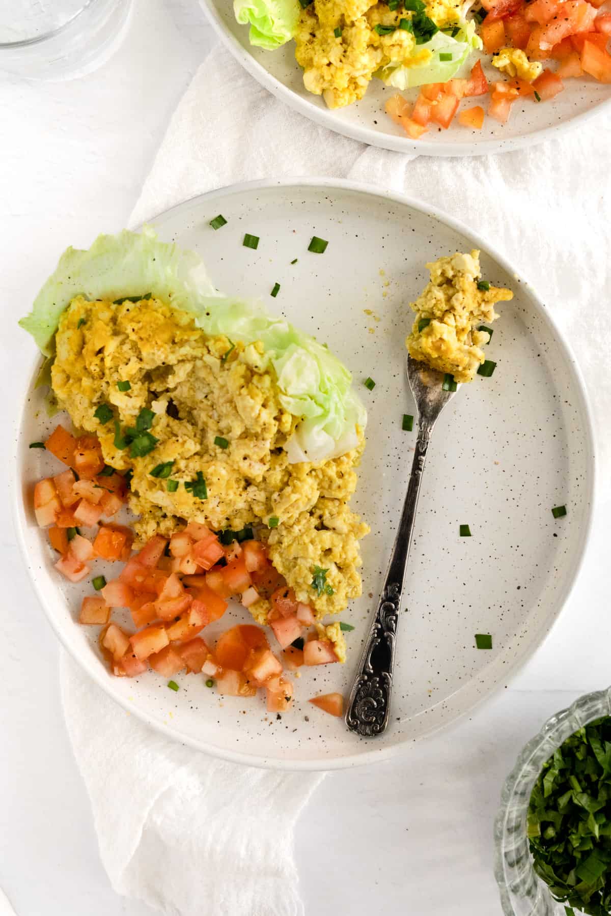 a white plate filled with yellow scrambled tofu, with a fork next to it and lettuce and tomato