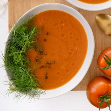 a white bowl of bright orange tomato and fennel soup garnished with fennel fronds