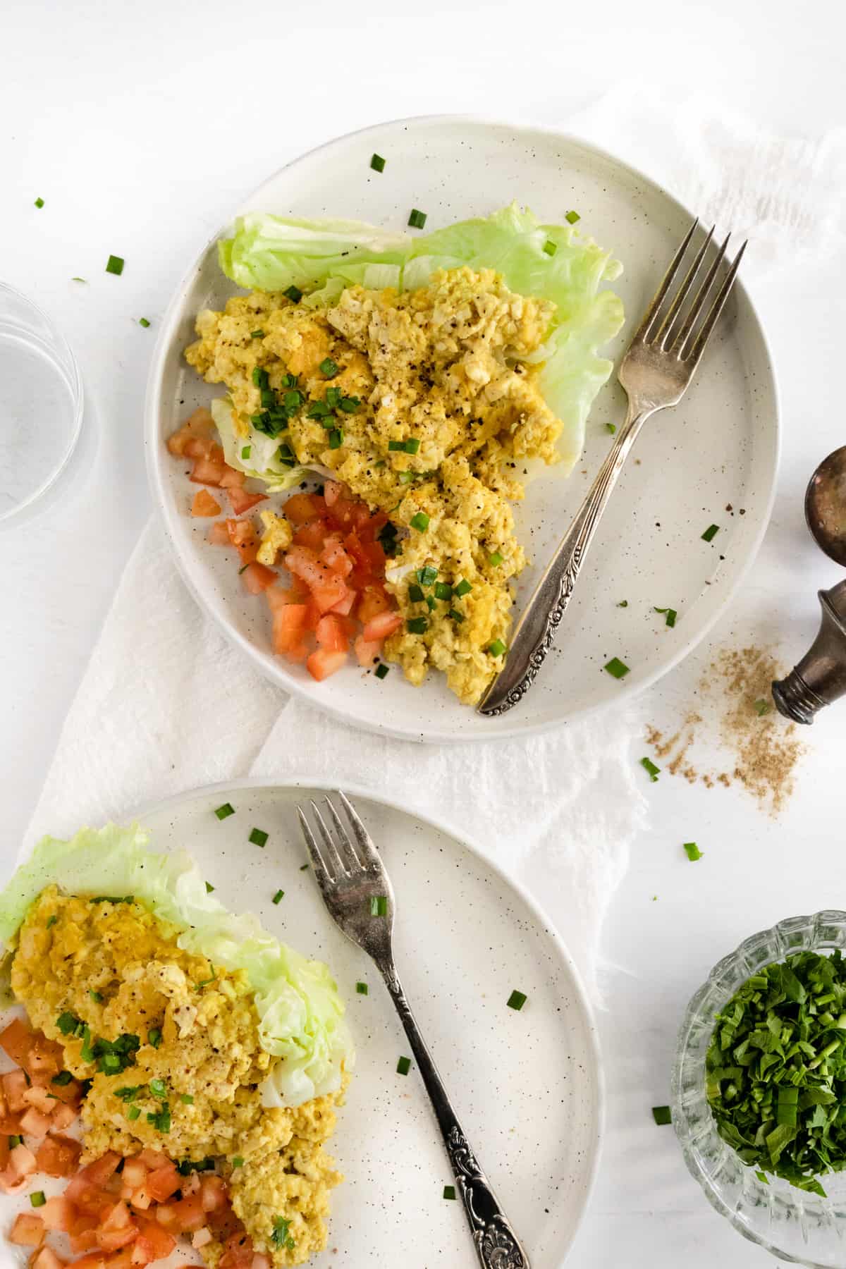 two white plates with scrambled yellow tofu in a green lettuce leaf with diced red omatoes