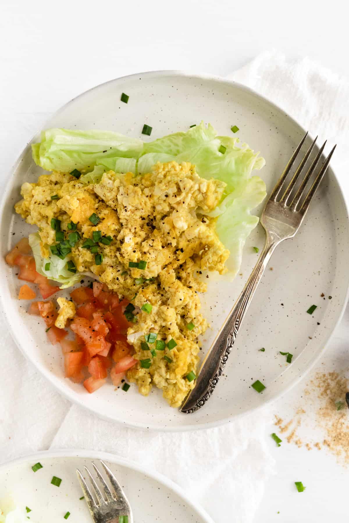 a white plate with a fork and lettuce, tomato and yellow scrambled tofu