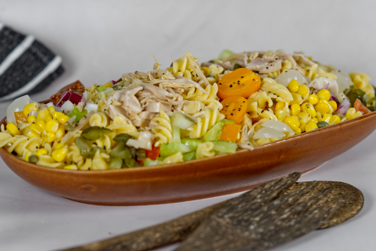 a pasta salad in a brown bowl with wooden serving utensils on the side