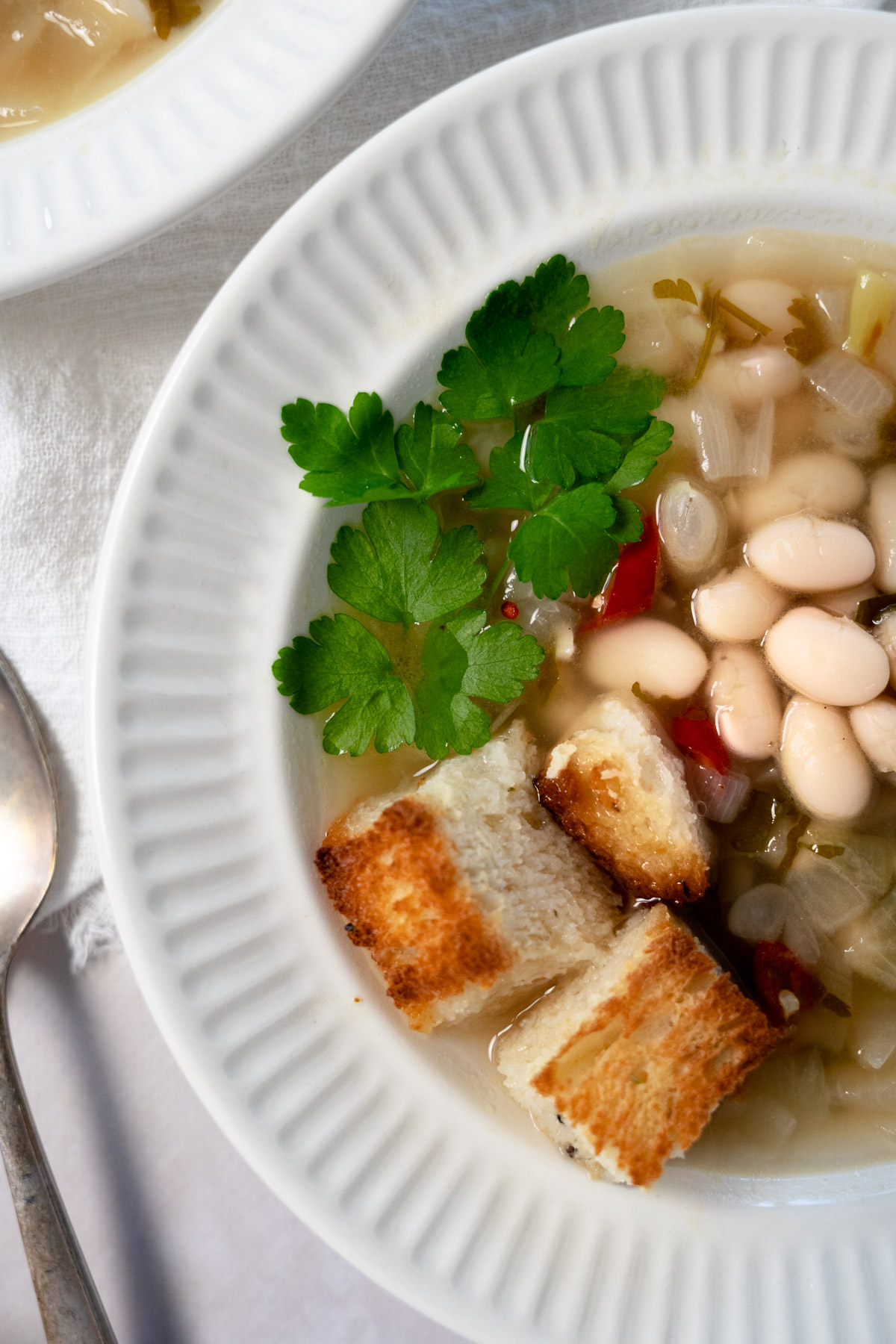 a white bowl of white bean soup with croutons