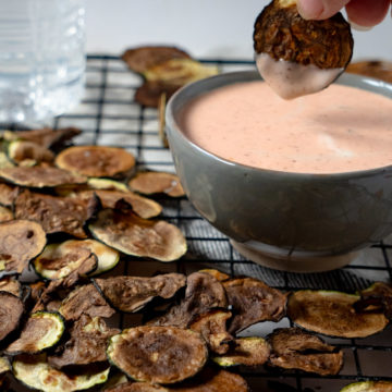 Zucchini chips on a wire rack with one being dipped into a pink sauce in the background