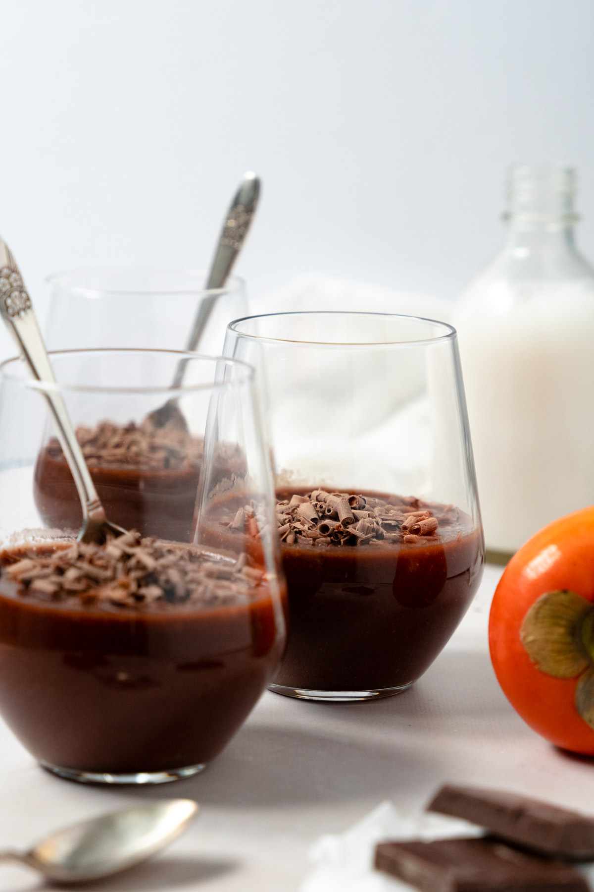 chocolate pudding in three cups with a persimmon on the side and a milk bottle in the background