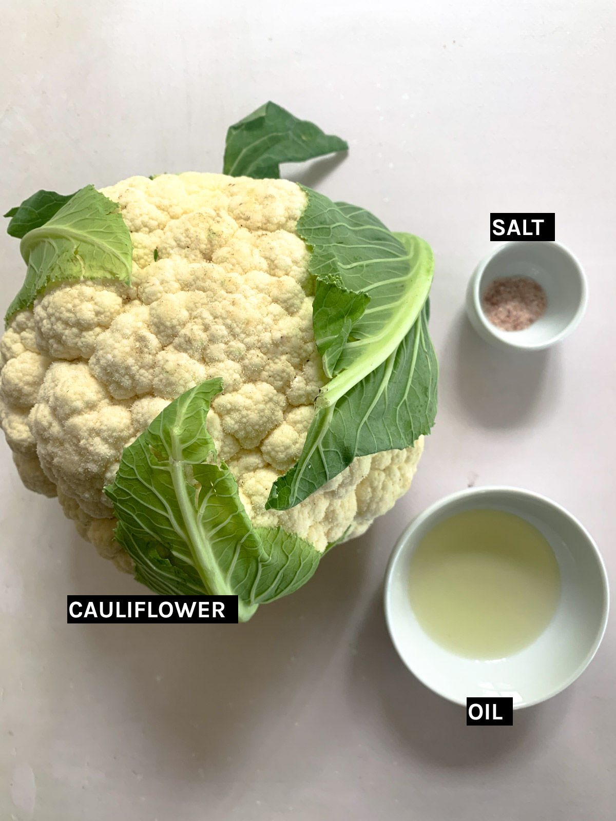 a head of cauliflower, separate white bowls of salt and oil