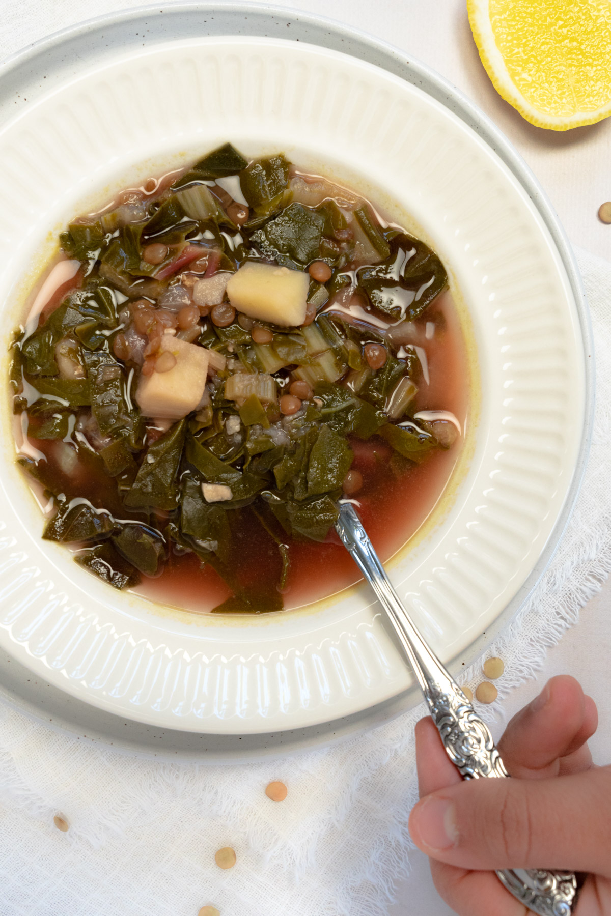 lemon lentil soup in a white bowl with a spoon held by a hand