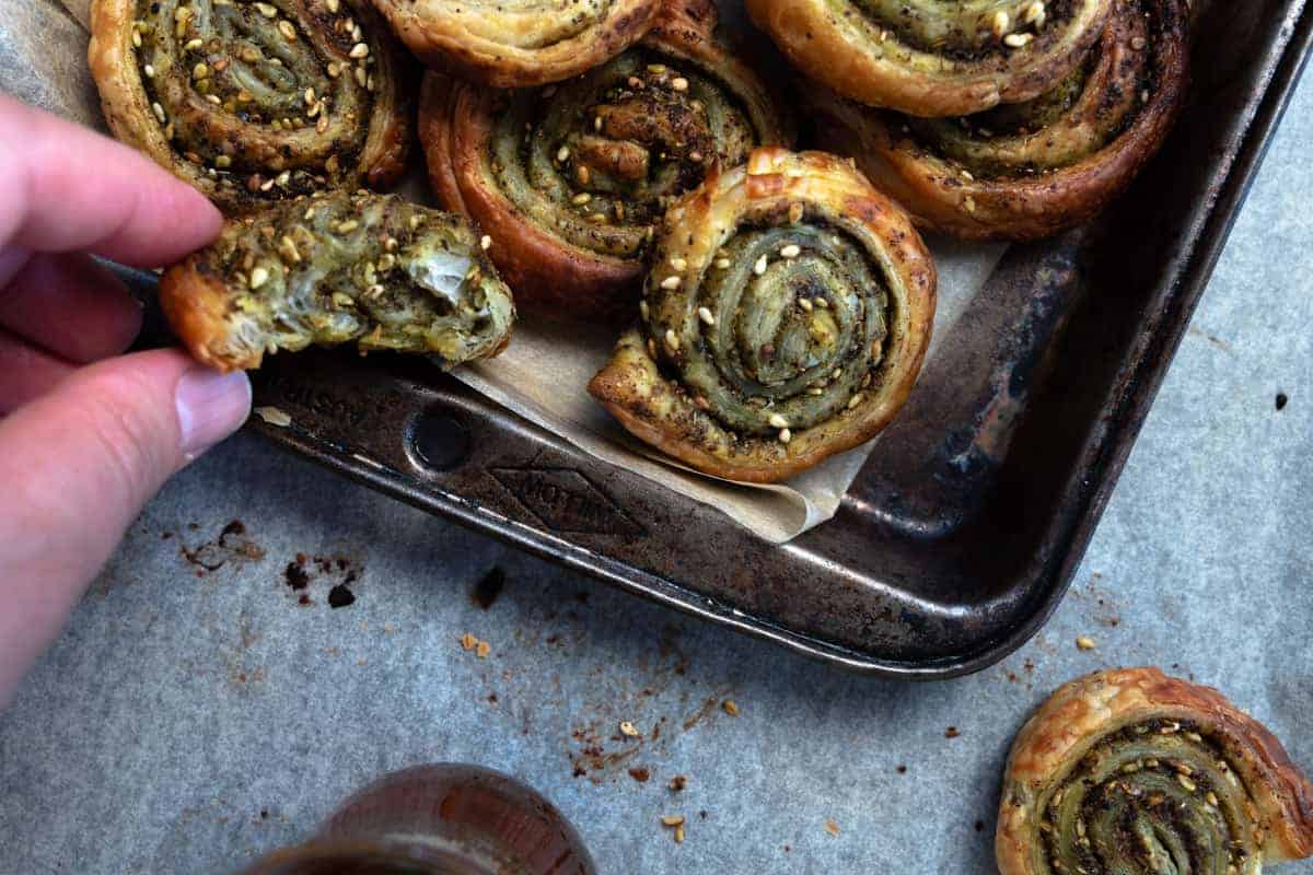 zaatar pinwheels in a tray with one held in a hand and a bite missing