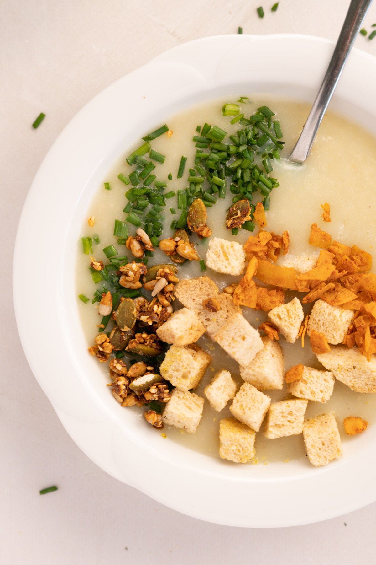 a close up of the white soup with  croutons, chives, seeds and coconut facon
