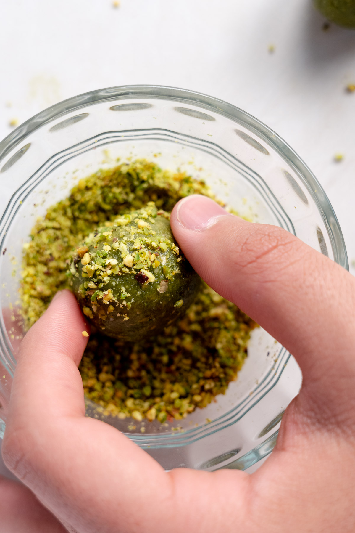 male hand rolling a matcha ball into crushed pistachio