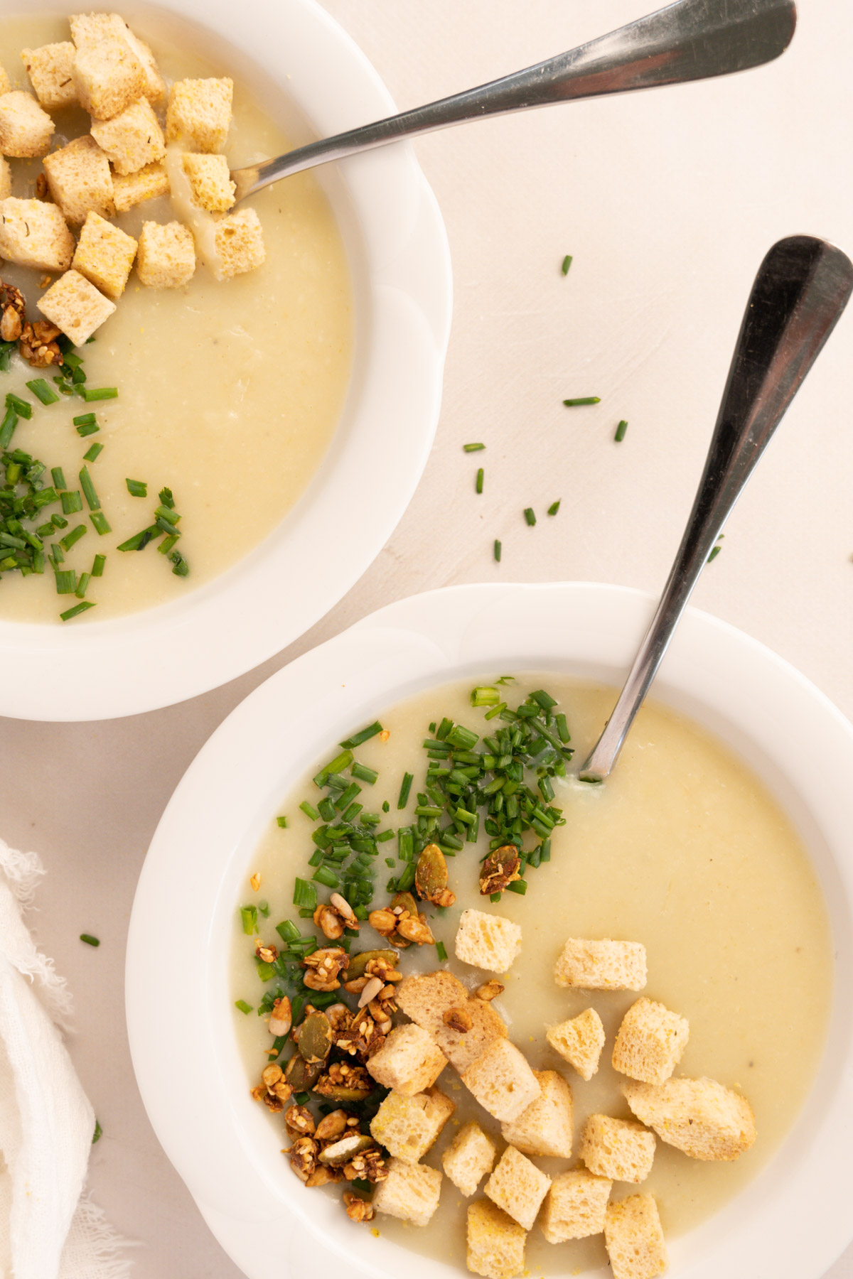 2 bowls of leek and potato soup with croutons, seeds and chives on top