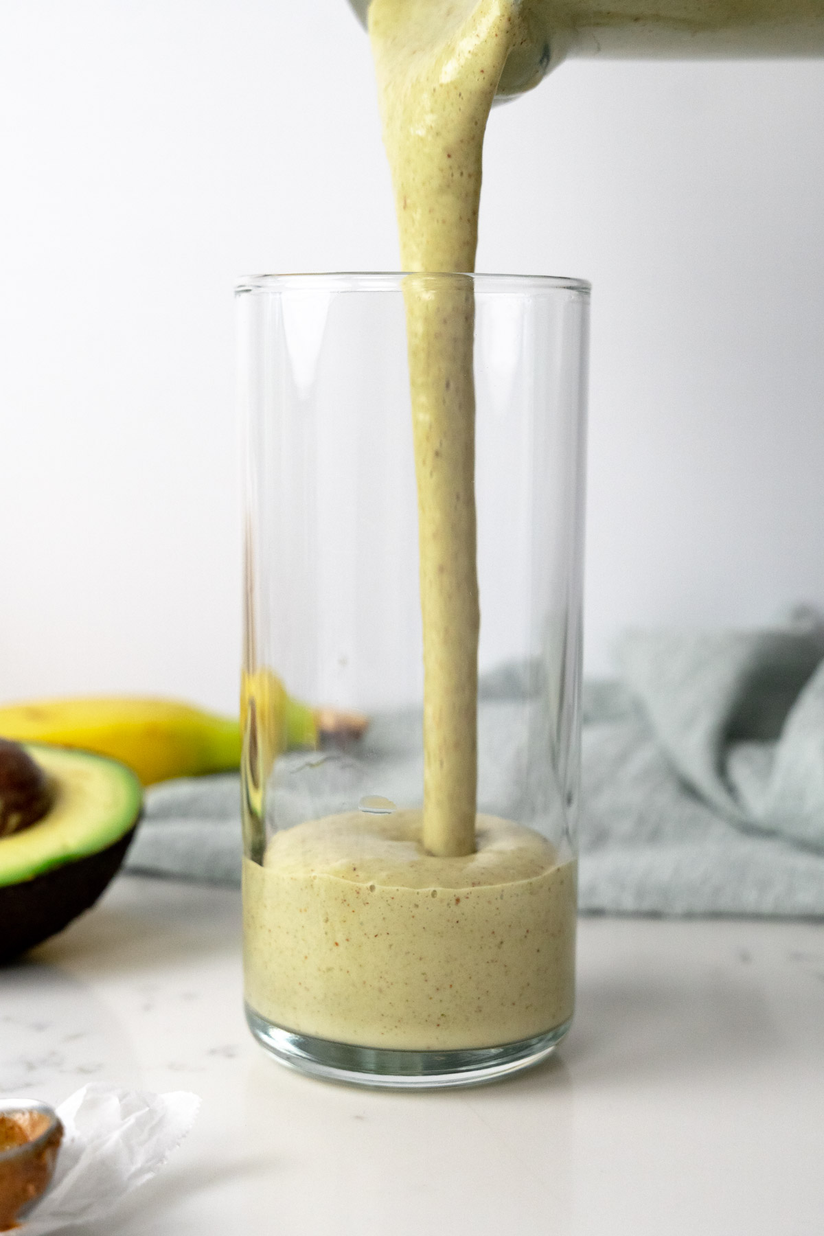 Banana avocado smoothie being poured into a glass cup