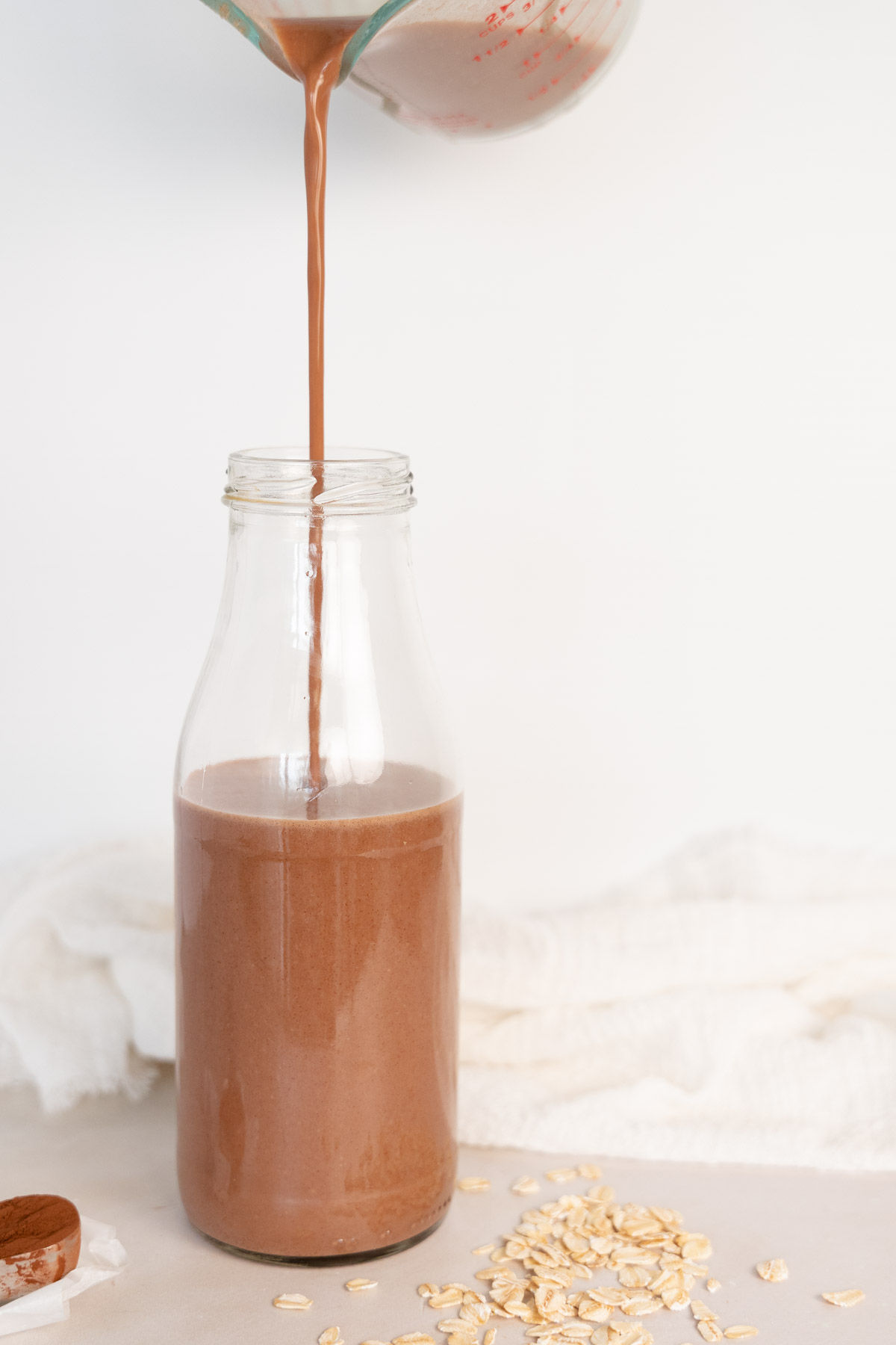 pouring chocolate oat milk into a glass bottle