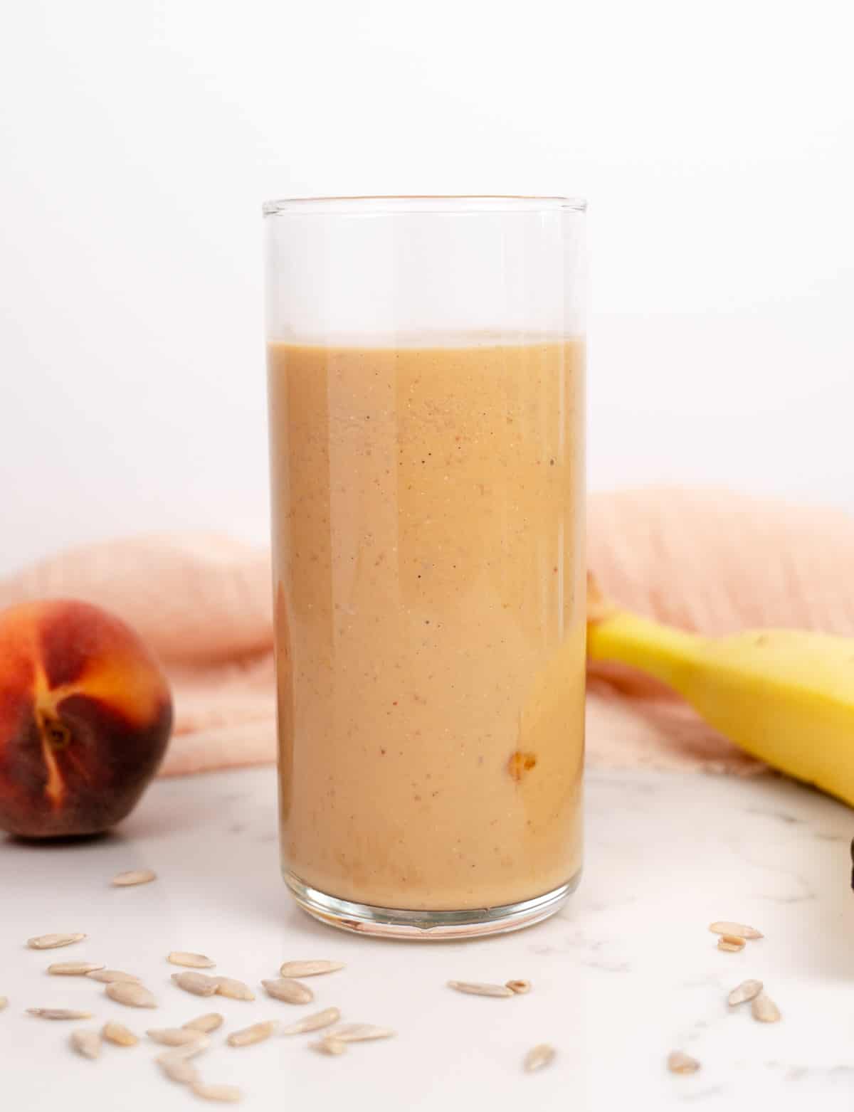 smoothie in a cup with a peach and banana laid next to it