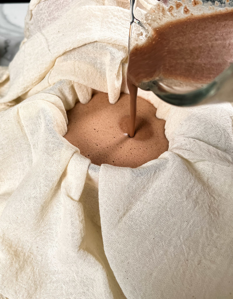 pouring chocolate oat milk into a cheesecloth