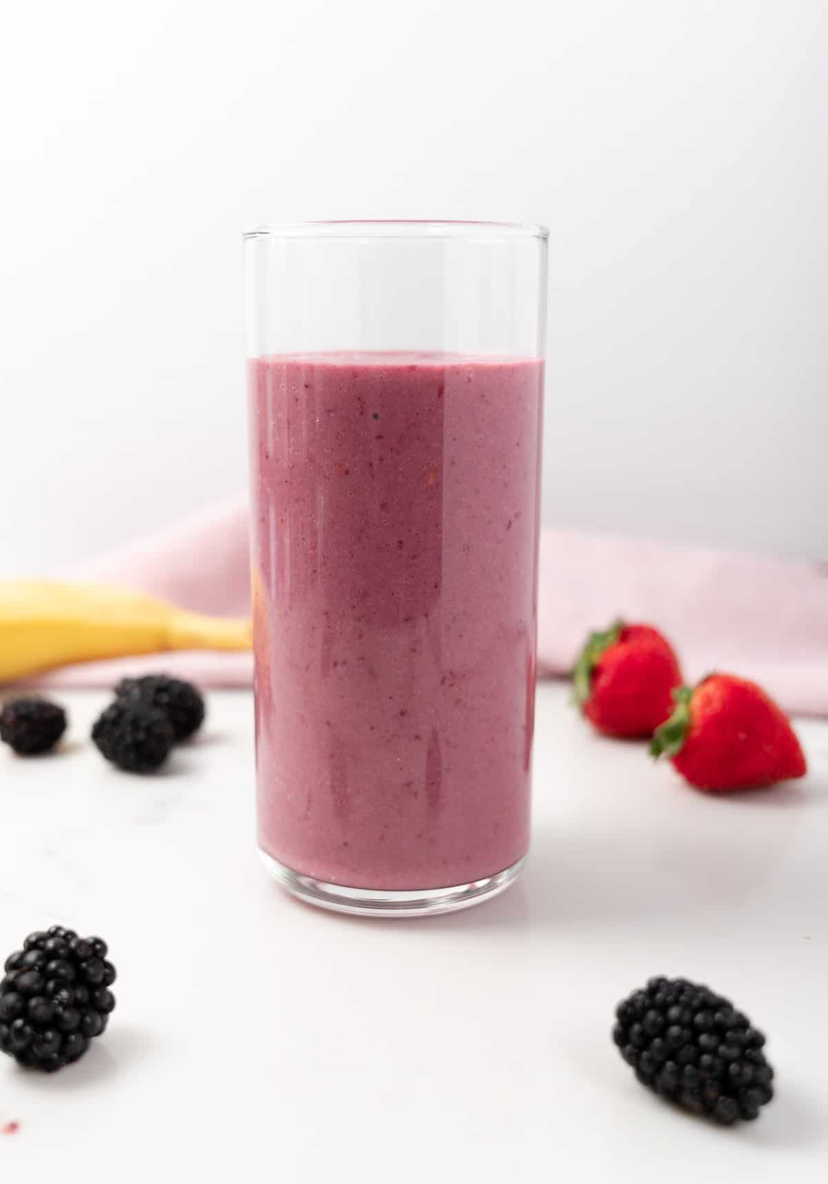 pin smoothie in a glass cup with berries scattered around