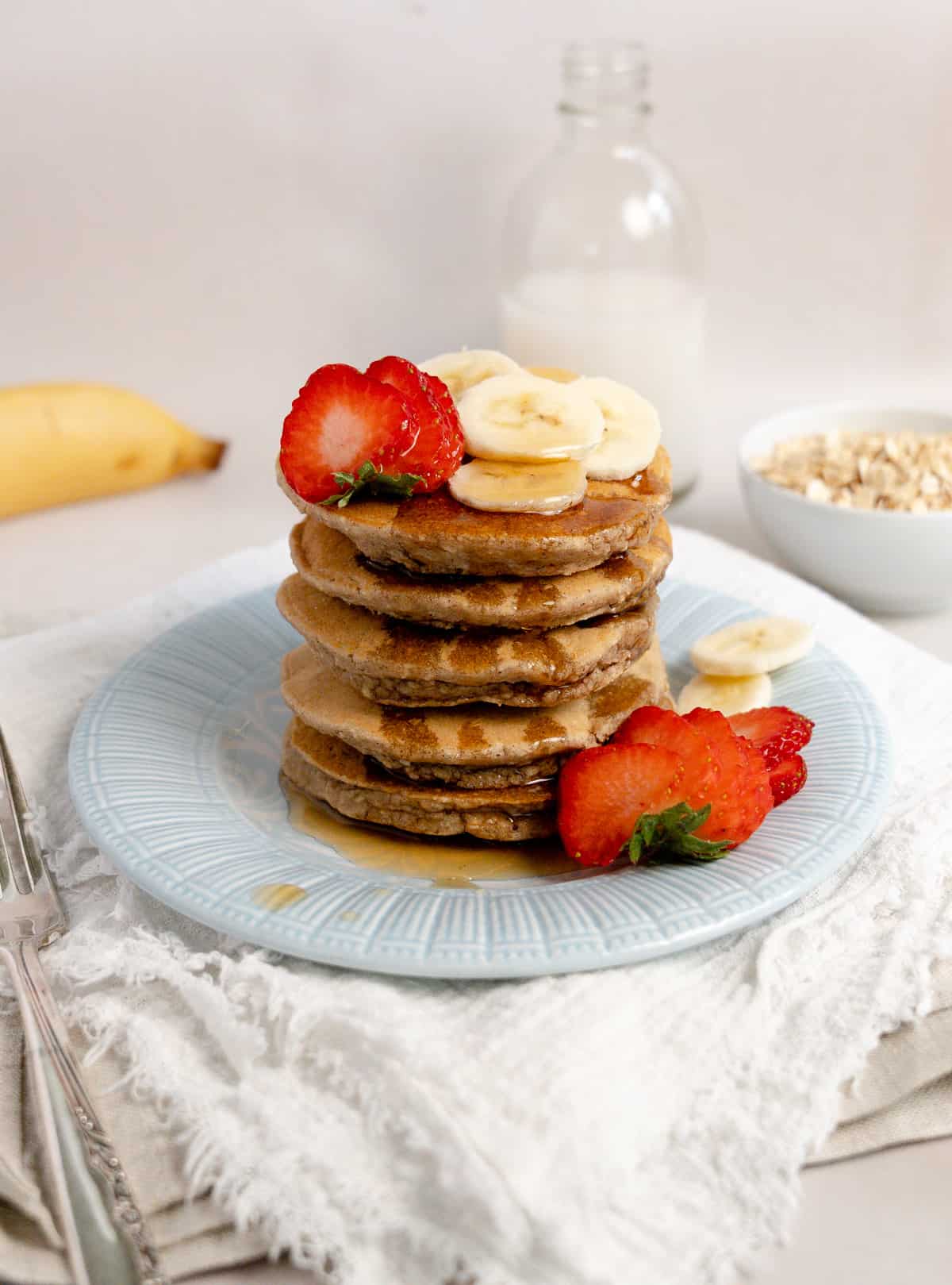 maple syrup soaked into a stack of pancakes with fruit on top and side