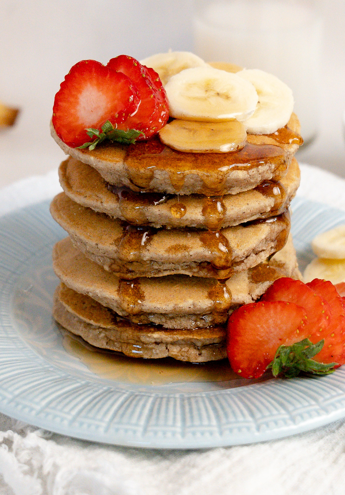 a stack of five pancakes with strawberries, banana and maple syrup