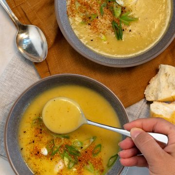 two grey bowl with yellow potato soup and spoons in them