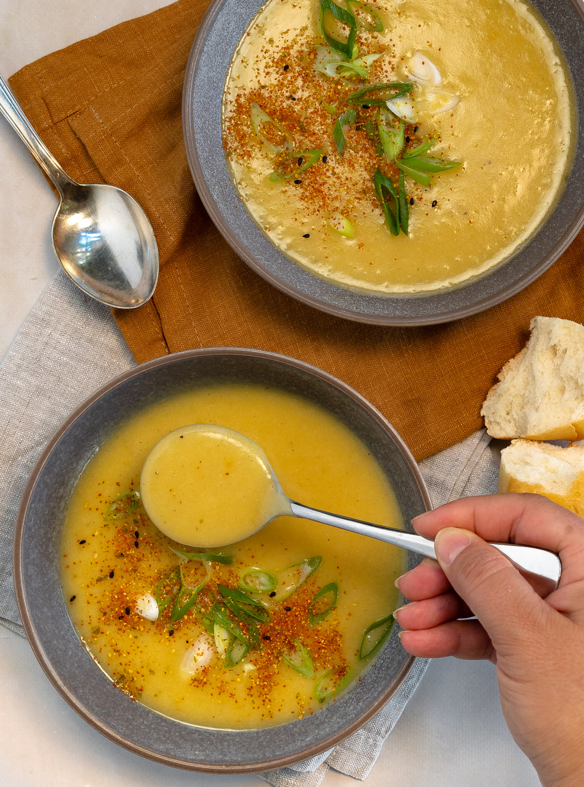 two grey bowl with yellow potato soup and and a female hand holding a spoonful