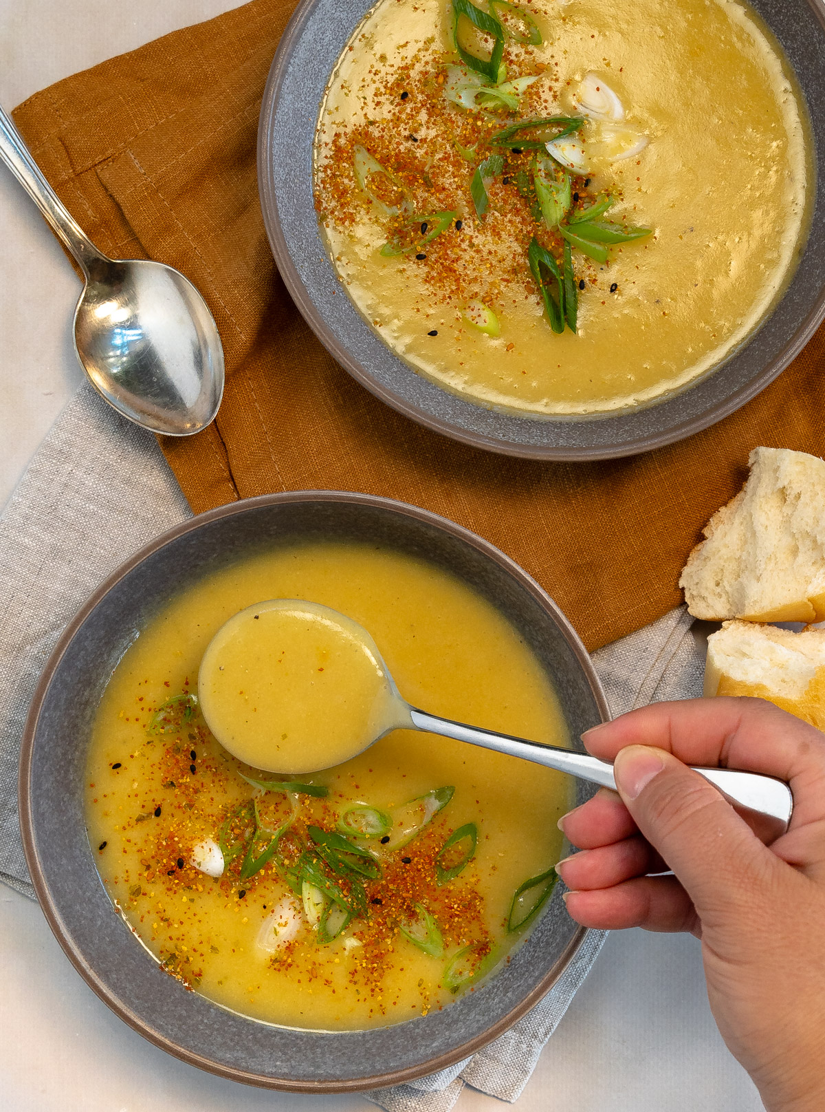 two grey bowl with yellow potato soup and spoons in them