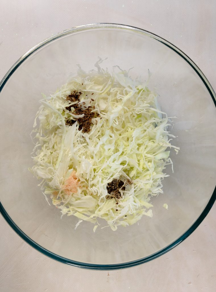 cabbage, caraway seeds, salt, black pepper in a glass bowl