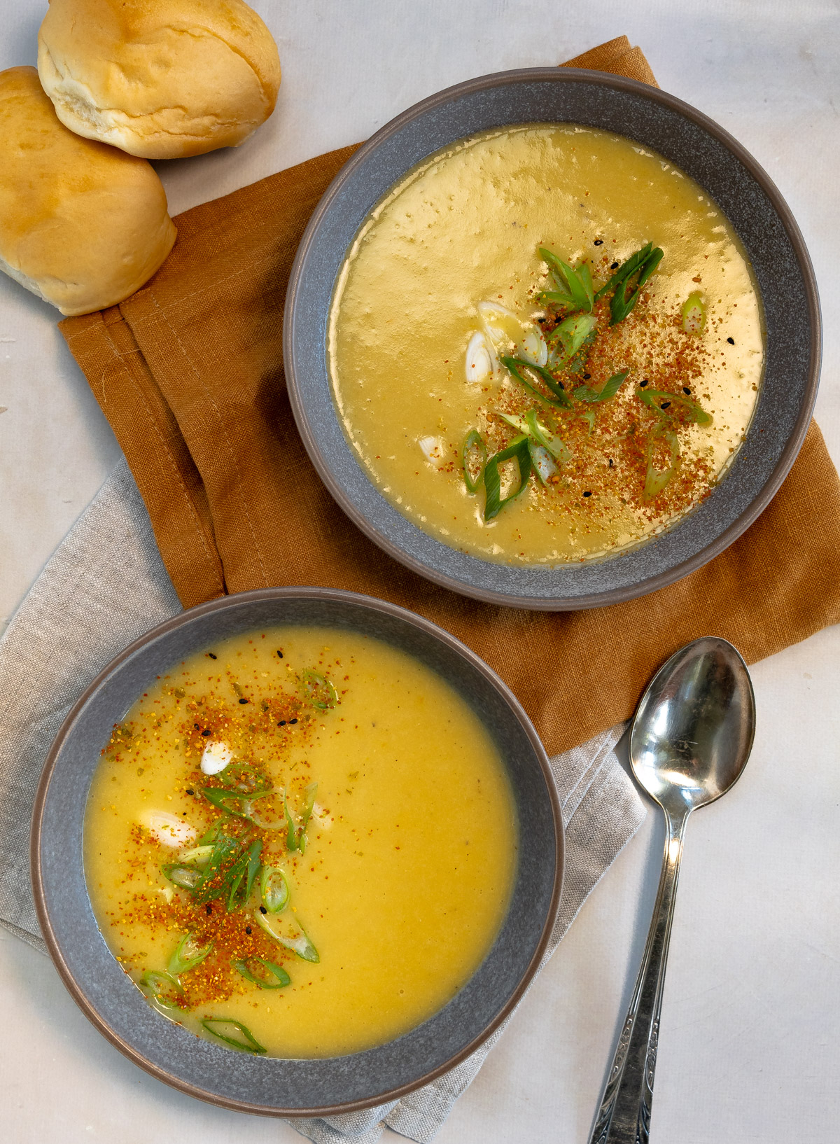 two bowls filled with soup and a couple of bread rolls on the side