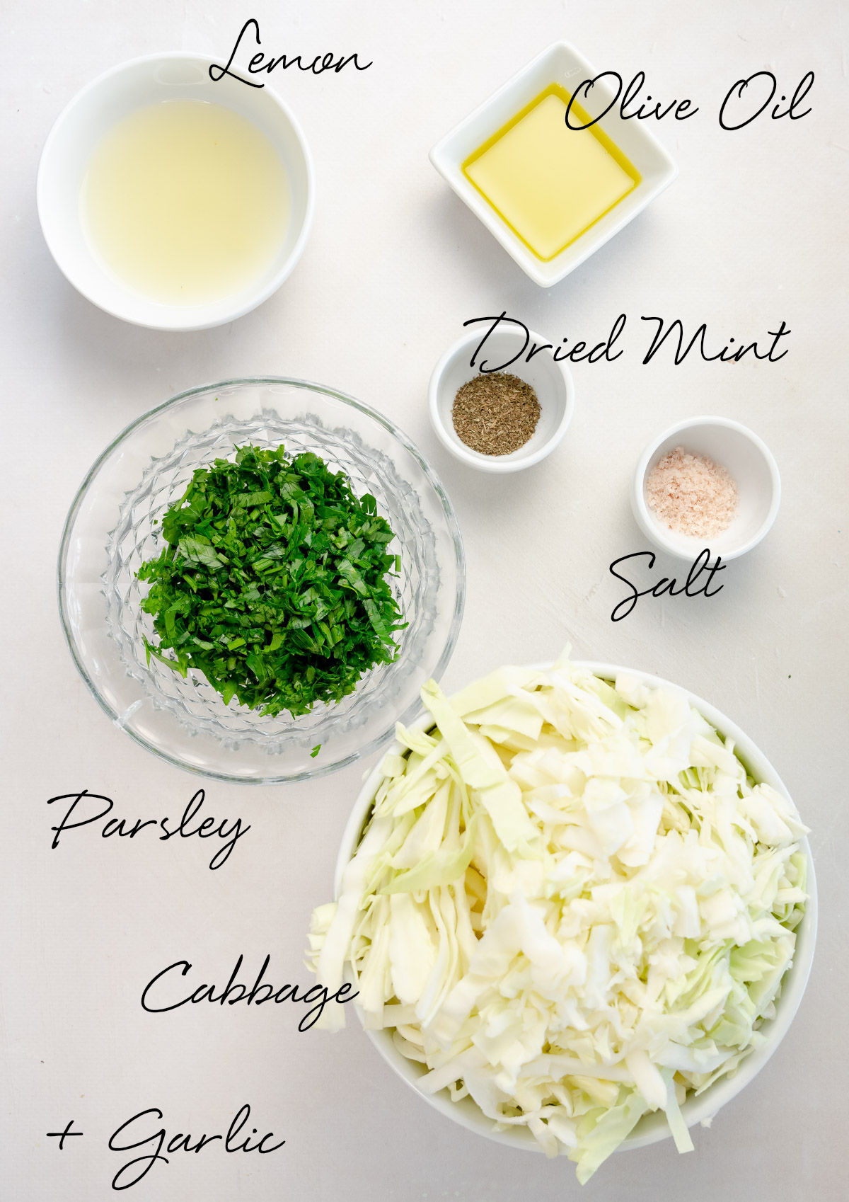 shredded cabbage, chopped parsley, lemon juice, oil, dried mint and salt in white bowls