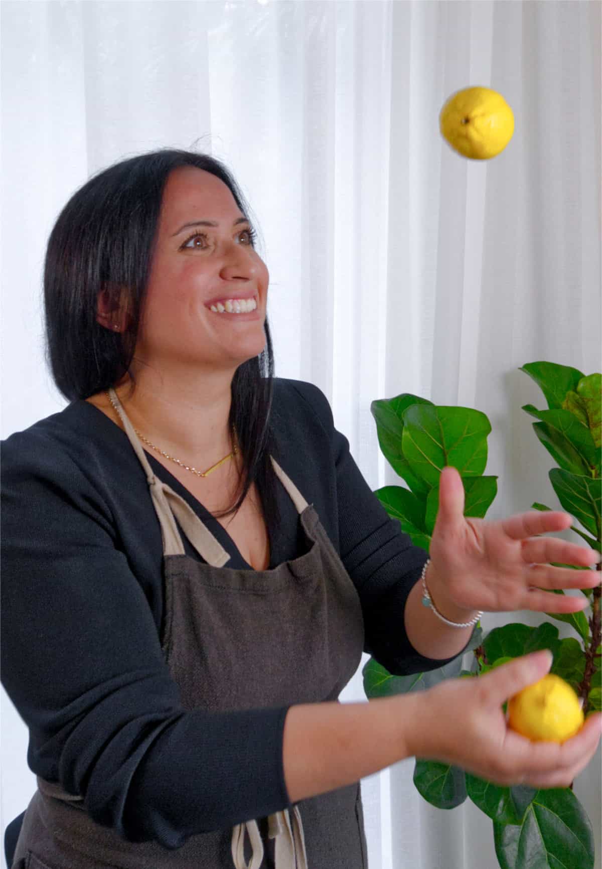 A female brunette dressed in black and an apron juggling lemons