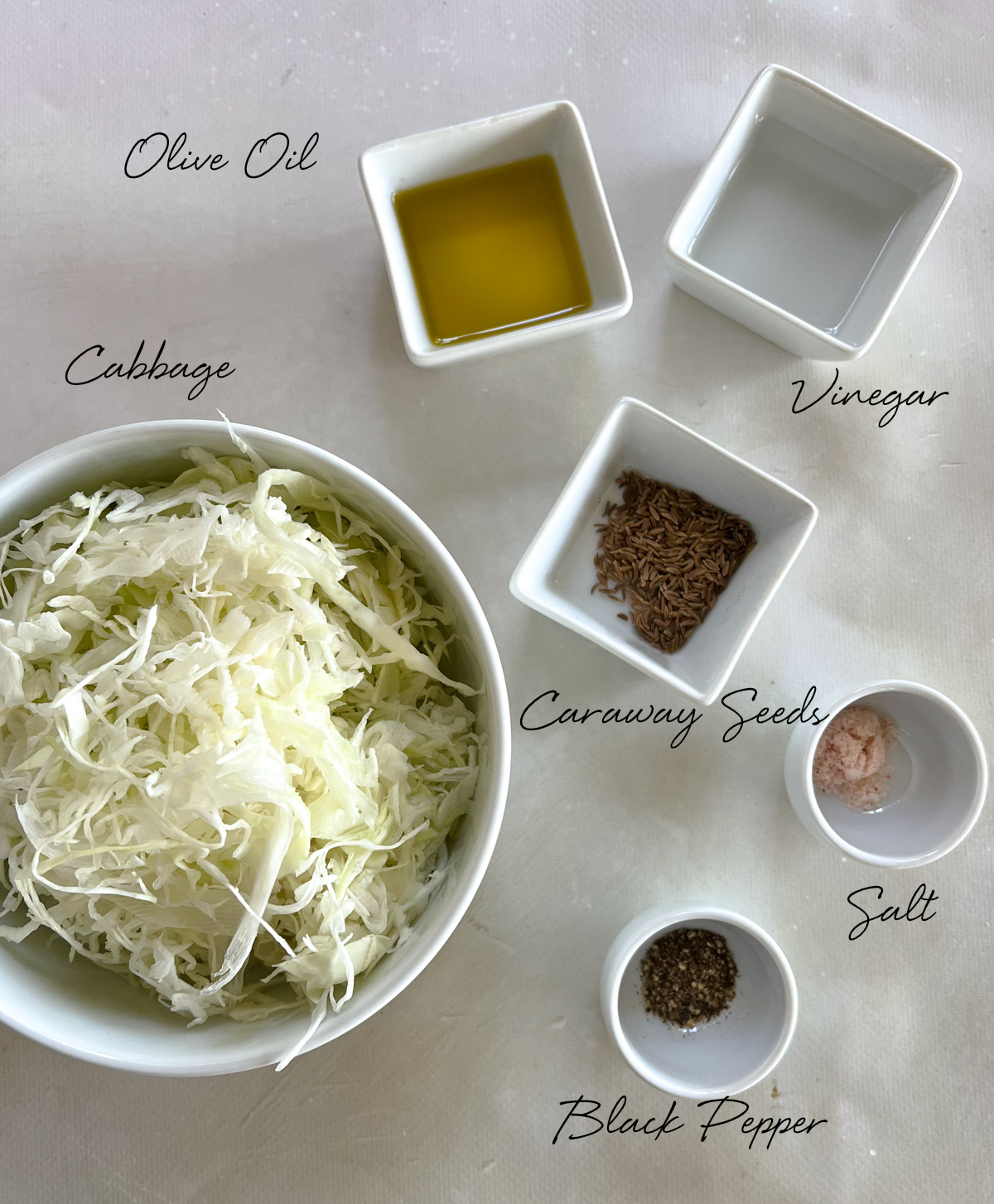 shredded cabbage, oilive oil, white vinegar, caraway seeds, salt and black pepper in white bowls