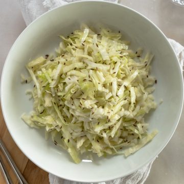 shredded cabbage salad with flecks of brown caraways seeds in a white bowl